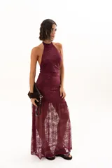 Vestido largo de encaje color bordó, con escote halter y diseño ajustado en el torso que se extiende hasta la cintura, donde continúa con una falda larga de encaje transparente.