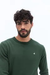 Sweater de punto color verde oscuro, con escote redondo, manga larga y calce regular. Presenta un pequeño logo bordado en el pecho.