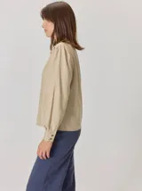 Camisa de denim con silueta levemente entallada, cuello bebé y mangas largas con sutil frunce en los hombros. Presenta costuras curvas decorativas con pespuntes en contraste y cierre frontal con botones.