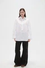 Camisa de algodón blanca de corte holgado, con cuello clásico, cierre frontal parcial con botones y mangas largas con puños anchos.