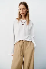 Pantalón recto color beige de tiro medio, con cintura elástica, bolsillos delanteros y cinturón ajustable con hebilla metálica dorada.