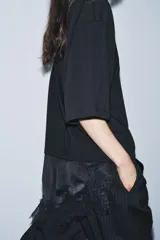 Camiseta de algodón de corte regular, color marrón oscuro o negro, con cuello redondo y manga corta. Presenta un bajo asimétrico con aplicación de encaje negro a tono.