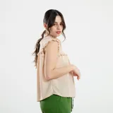 Camisa sin mangas color beige, con cuello alto con volados, detalles de encaje calado en los hombros y parte superior del pecho, y cierre frontal con botones.