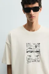 Camiseta de corte relajado color crudo, con cuello redondo y manga corta. Presenta un estampado gráfico en el frente con motivos de palmeras y paisajes en color negro.