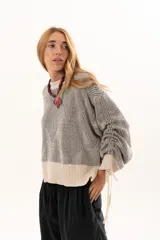 Buzo de tejido de punto con diseño geométrico en relieve, cuello redondo y mangas largas abullonadas con puños ajustables mediante lazos. Presenta un borde inferior en tejido acanalado de color crudo.