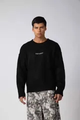Sweater de punto acanalado color negro, con cuello redondo, mangas largas y calce holgado. Presenta una pequeña estampa gráfica en el centro del pecho.
