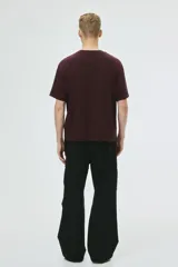 Remera de punto de algodón de peso medio color bordó, con cuello redondo ribeteado, hombros caídos y bajo recto. Presenta un diseño estampado circular en el pecho con texto y un arco. Corte holgado.