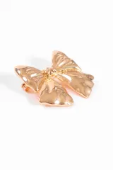 Broche prendedor con forma de moño dorado con textura irregular.