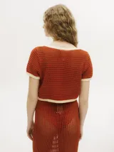 Top de tejido calado con cuello en V, mangas cortas y cierre frontal con botones carey. Presenta detalles de ribetes en color contrastante en el cuello, puños y ruedo.