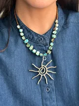 Collar corto con dije central en forma de sol de metal, engarzado en una cadena compuesta por cuentas de nácar turquesa y mostacillas marrones.