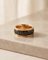 Anillo de acero con baño dorado y diseño ancho, con incrustaciones de circonias negras talladas en forma de baguette en todo su contorno.