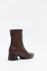 Bota corta de caña media color marrón oscuro, con puntera cuadrada y taco medio geométrico con textura acanalada. Presenta cierre de cremallera en la parte trasera y un ajuste tipo calcetín en la caña.