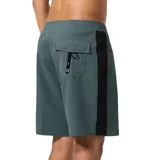 Boardshort de surf de 19 pulgadas, color verde azulado oscuro, con franja vertical negra en el lateral y cordón de ajuste negro en la cintura. Presenta un pequeño parche con el logo de la marca en la parte inferior del lateral derecho.