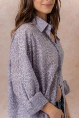 Camisa lila oversize de algodón con bordado floral calado tipo broderie, cuello camisero, manga larga y abotonadura frontal.