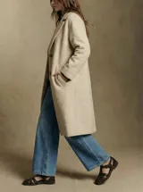 Tapado largo color beige claro, de corte oversize, con cuello solapa y cierre frontal de botones.
