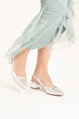 Zapato plateado de cuero sintético con punta fina, talón descubierto y taco cuadrado bajo.
