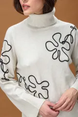 Sweater de punto color azul marino con cuello alto y diseño holgado. Presenta mangas con hombros caídos, terminaciones acanaladas y apliques de líneas orgánicas en relieve de color blanco que forman figuras florales en el frente y las mangas.