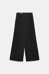 Pantalón negro de tiro alto con diseño cruzado tipo pareo, pinzas delanteras y pernera ancha. Cuenta con cierre lateral de cremallera oculta.