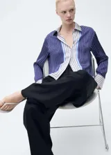 Camisa de tejido fluido con acabado satinado, diseño de rayas verticales en tonos azul marino, blanco y celeste. Presenta cuello camisero, cierre frontal con botones y mangas largas con puños abotonados.
