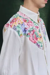 Camisa de corte oversize con mangas largas y puños abotonados. Presenta un diseño bicolor con cuerpo blanco y un canesú delantero con estampado floral multicolor.