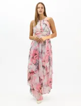 Vestido largo de fiesta con estampado floral en tonos rosa y gris sobre fondo blanco. Presenta cuello halter con abertura tipo lágrima, cintura drapeada y falda amplia con capas asimétricas y bajo en picos. Confeccionado en tejido ligero con forro interior.