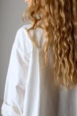 Camisa blanca de corte clásico, con cuello camisero y mangas largas con puños abotonados.