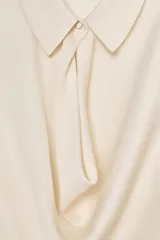 Blusa de tejido satinado color bordó, con cuello solapa, manga larga y detalle de abertura drapeada en el pecho. Cuenta con cierre frontal mediante un botón forrado.