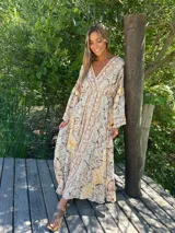 Vestido largo de seda con estampado paisley en tonos beige, rosa, amarillo y marrón. Presenta escote en V, mangas 3/4 acampanadas y corte fluido.