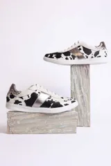 Zapatillas deportivas con estampado animal print de vaca en blanco y negro, con detalles en cuero sintético plateado en los laterales y talón.