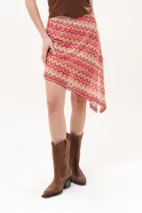 Pollera midi de corte asimétrico con tejido de crochet y patrón en zigzag multicolor en tonos rojo, rosado y beige.
