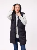 Chaleco largo acolchado color negro, con capucha, cierre frontal y botones a presión. Diseño sin mangas con acabado técnico.