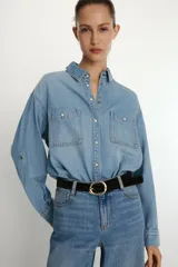 Camisa de denim de corte oversize con cuello solapa, manga larga con puños, cierre frontal con botones a presión y bolsillos de plastrón en el delantero.