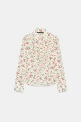 Camisa entallada de manga larga con estampado floral en tonos rosados y azules sobre fondo crema. Presenta cuello solapa, puños abotonados y volantes decorativos en el frente, con cierre de botones.