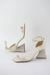 Sandalias color crema con tira delgada sobre los dedos, pulsera al tobillo con hebilla y taco geométrico.