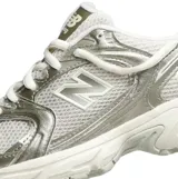 Championes New Balance modelo 530, con diseño retro inspirado en el running. Presenta una estructura de malla transpirable con revestimientos sintéticos en tono dorado metálico. Cuenta con entresuela con tecnología ABZORB para una amortiguación superior y suela de goma resistente.