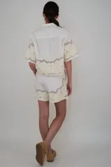 Short blanco de lino con cintura elastizada y ajuste con cordón. Presenta apliques de flores bordadas en el ruedo.