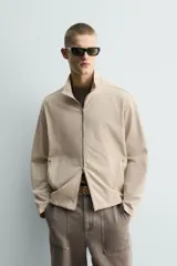 Sudadera de algodón color beige claro con efecto lavado, corte relajado, cuello alto y cierre frontal de cremallera. Presenta bolsillos de vivo en la cadera y mangas largas.