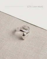 Anillo de acero quirúrgico plateado, de diseño abierto y ajustable, con detalle de gota en el frente.