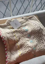 Sweater de hilo de algodón color beige, de diseño holgado con hombros caídos, tejido de ochos y detalles bordados a mano en varios colores.