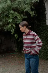 Remera de manga larga con cuello polo y cierre frontal de botones. Presenta un diseño a rayas horizontales en tonos bordó, blanco y celeste.