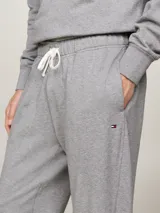 Pantalón de jogging gris de felpa de algodón, con cintura elástica ajustable con cordón, dos bolsillos laterales, un bolsillo trasero y bajos elásticos. Presenta el logo de Tommy Hilfiger bordado en el lateral.