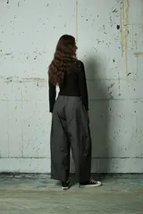 Pantalón de corte holgado y tiro alto en color gris oscuro, con pinzas frontales y costuras verticales decorativas a lo largo de las piernas.