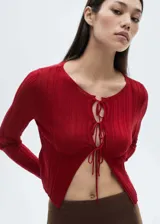 Cardigan de punto fino color rojo, con diseño corto, cuello redondo y manga larga. Presenta un cierre frontal mediante múltiples lazos finos.