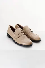 Mocasín color marrón claro, con capellada de cuero liso y aplique de gamuza en marrón oscuro. Tiene punta redondeada y suela plana de goma negra.