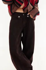 Pantalón de jean tipo balloon de tiro bajo, color marrón oscuro. Presenta un diseño con recortes curvos en las piernas, cierre frontal con doble botón en la cintura y costuras reforzadas.