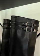 Botas de caña alta color negro, con diseño de estilo western y punta fina. Presentan doble correa superior con hebillas metálicas y detalles de tachas, además de una abertura lateral en la caña y taco cuadrado.