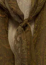 Blusa de tejido fluido con estampado paisley en tonos verdes y marrones. Presenta escote en pico con detalle de lazo, mangas largas abullonadas con puños abotonados y diseño recto.