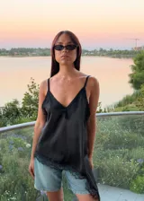 Blusa tipo lencera de satén negro con breteles finos, escote en V y detalle de encaje en el escote y en el ruedo asimétrico.