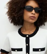 Cardigan de punto de manga corta con cuello redondo y cierre frontal de botones perolados. Presenta un diseño bicolor en blanco y negro con detalles de contraste en cuello, puños, tapetas de bolsillos frontales y vista central.