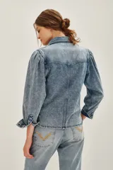 Camisa de jean de corte clásico con efecto lavado, cuello camisero, cierre frontal con botones metálicos y bolsillos frontales con solapa. Presenta mangas largas con diseño abullonado en los hombros y puños abotonados.